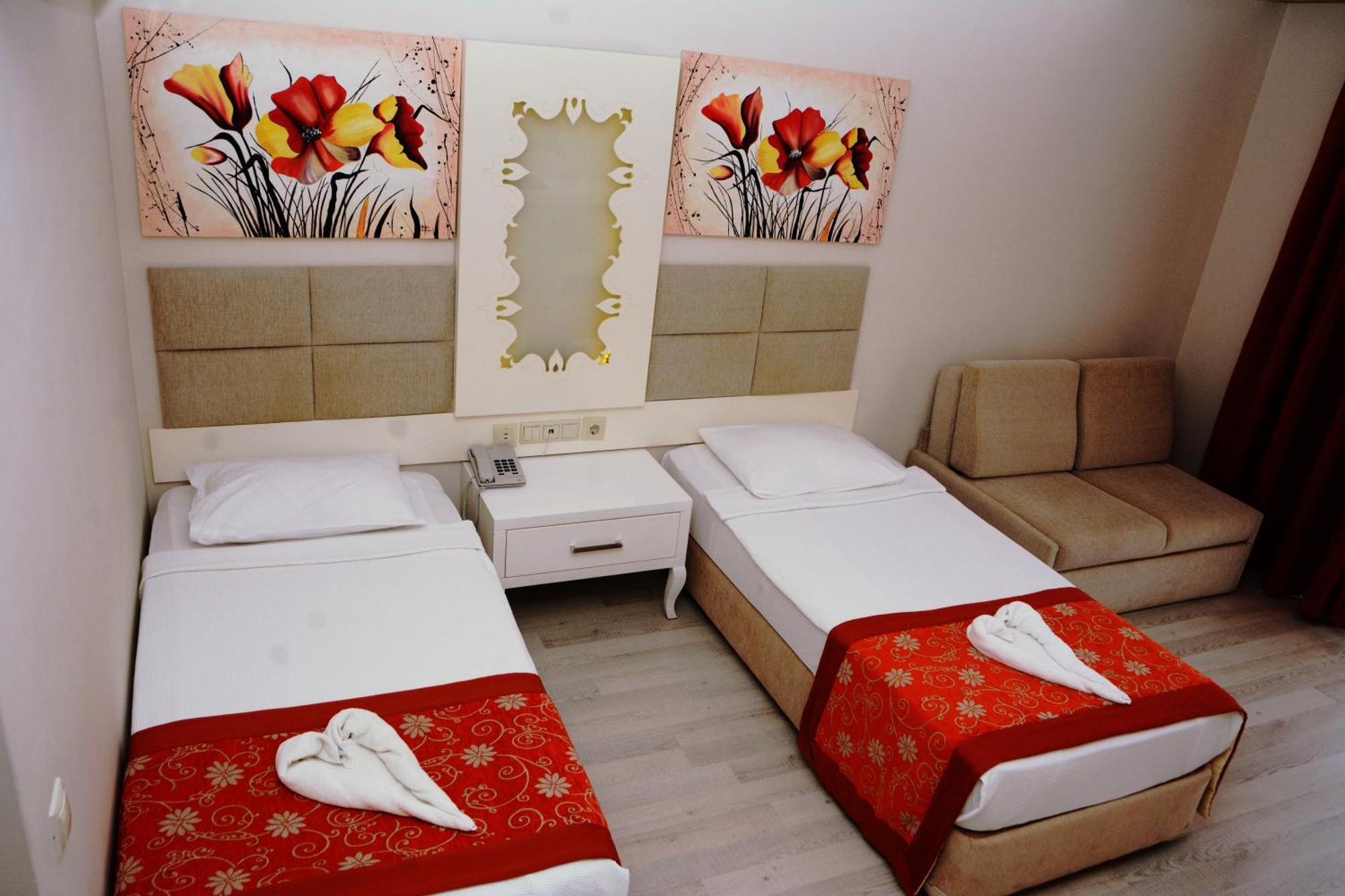 Miramor Hotel & Spa أنطاليا المظهر الخارجي الصورة The photo shows a hotel room featuring two single beds with white linens, each adorned with a decorative red throw. The headboards are upholstered in a light beige fabric. Above the beds, there are two large artwork pieces depicting colorful flowers.