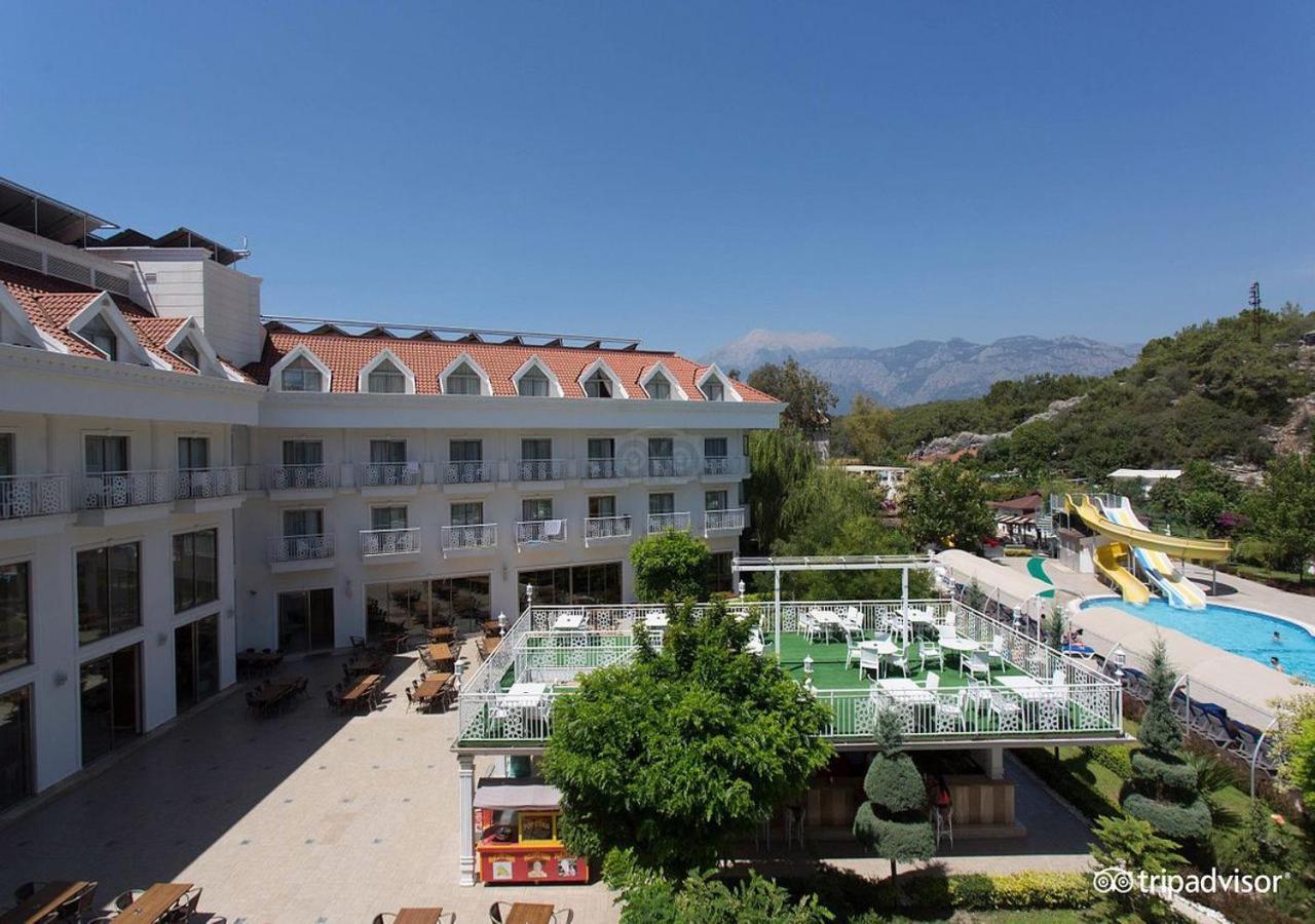 Miramor Hotel & Spa أنطاليا المظهر الخارجي الصورة The photo shows a hotel or resort facility with a well-maintained exterior. There is a large green area with grass and some trees, likely intended for relaxation or recreational activities. In the background, there are water slides suggesting an amus